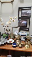 Photo showing various items on table including brass candleholders, metal bamboo-like frame with faux orchids, votive holder, planter, and three-photo frame.