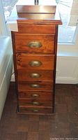 Front view of tall wooden cabinet showing six drawers with metal pull handles and scratches on wood surfaces