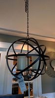 Full view of the spherical metal chandelier hanging from ceiling with visible chain and battery-operated candle lights inside.