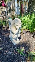 Full view of the cement gargoyle statue in a garden setting showing the front and wings.