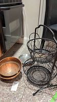 Photo showing 2 copper plated bowls, 1 metal crepe pan and two-tiered black metal storage basket.