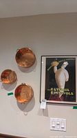 Three copper plated pans hanging on wall next to the framed Italian print