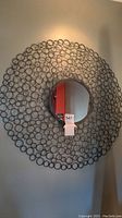 Full view of the circular decorative metal mirror hung on a wall, showing intricate concentric circle pattern and central mirror