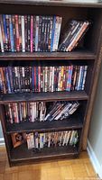 Wooden bookshelf filled with DVDs arranged in rows across four shelves.