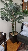 Artificial palm tree displayed in corner of room next to furniture, showing full height and planter