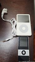 White Apple iPod Classic with earbuds and black MP3 player on dark wood surface