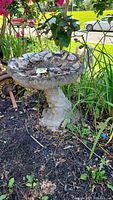 Full view of the birdbath installed in garden soil, mosaic flower pattern in basin visible but dirty.
