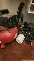 Red Porter Cable air compressor tank with black motor housing and motor on top alongside pneumatic tool attachments on floor.