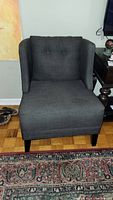 Front view of the dark gray tweed wingback side chair with button tufted backrest and wooden legs.