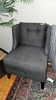 Full view of dark gray tweed side chair with pillow top cushion and winged sides, wooden legs visible.