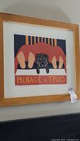 Framed wall art print titled "Ménage à Trois" showing two pairs of feet and a dog lying on a bed.
