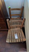 Two vintage wooden children's chairs with wood slat seats and ladder backrests shown stacked.