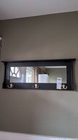 Full front view of the wood framed mirror with hooks mounted on a wall.