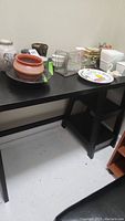 Black wooden desk with two shelves on one end, some decorative pottery on top (not included)