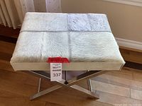 Full view of bench showing chrome base and animal skin upholstered seat divided into four stitched squares.