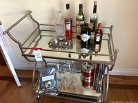 Full front view of the metal bar cart with items on top and bottom shelves showing bottles, decanter, glasses, and books.