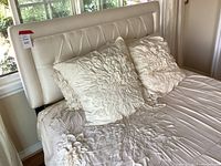 Full view of the bed showing padded upholstered cream frame and floral textured bedding with pillows.