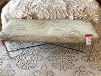 Full view of bench showing chrome frame and animal skin upholstered seat on patterned rug.