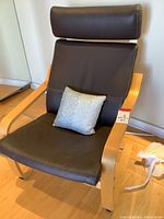 Front and side views of a black leather chair with wooden frame and curved armrests, with a gray pillow on the seat.