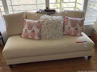 Front view of cream-colored armless wide sofa chaise with three decorative pillows on it.