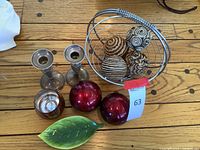 Photo showing two sterling silver candlesticks, wire basket with fabric balls, red glass balls, and green leaf dish on wooden surface
