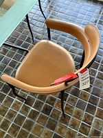 Close-up of tan leather seat and curved backrest with white stitching on black metal frame