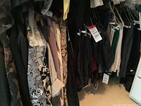 Wide view of clothing rack with assorted dark and floral pattern tops, blouses, dresses mostly in small and medium size with tags on some items.