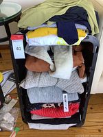 Stacked ladies clothing including sweaters, coats, tops in various colors and patterns. Tag with lot number visible.