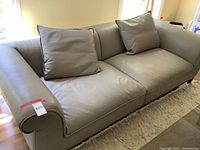 Full view of sofa showing rolled arms, two loose back pillows, leather upholstery
