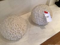 Two spherical white flower-shaped battery operated lights placed on a white surface, showing their textured petal design.