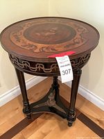 Full view of the antique round wooden side table showing metal filigree around edges and tripod base with metal accents.