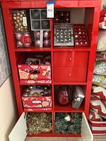 Full view of red shelf filled with Christmas ornaments, fabric boxes, tinsel garlands, and decorative items.