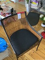 Overview of both chairs showing wicker chair in front and wire chair behind on wood floor.