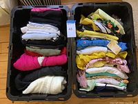 Two large bins filled with folded women's clothing in a mix of colors including bright pink, black, white, blue, yellow, and patterned pieces.