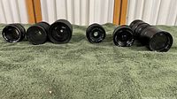 Wide view of all seven camera lenses displayed on green towel, showing varying sizes and barrel designs.