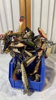 Tangled pile of mixed fishing lures in blue bin, various shapes, sizes, colors