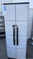 Front view of the white plastic storage cabinet with two black handles and a locking mechanism on one door.