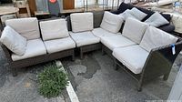 Full view of L-shaped modular outdoor patio sectional couch with beige cushions outside on pavement.