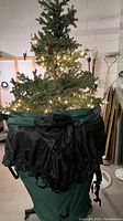 Artificial Christmas tree partially inside its green and black rolling storage cover with some lights illuminated.