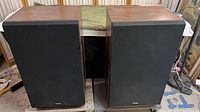 Two vintage Fisher ST-845 speakers side by side, covered by black fabric grills and wood veneer casing.