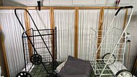 Two rolling foldable shopping/errand carts side by side flanked by a folded padded moving blanket.