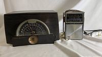 Photo showing two vintage General Electric radios side by side on a white surface; one rectangular tabletop AM radio with large circular dial, the other a portable AM/FM two-way radio.