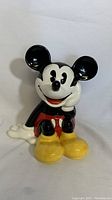 Front of vintage Disney Mickey Mouse cookie jar showing seated figure with a hand resting on the cheek, yellow shoes, and red shorts.