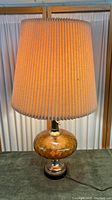 Full view of vintage amber hammered glass lamp with beige pleated fabric shade lit up