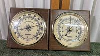 Front view showing both thermometer and barometer in wooden frames with glass and brass rims.