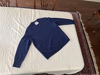 Cobalt blue cashmere sweater laid flat on a white surface, showing full sweater front and sleeves extended with visible texture and color.