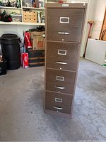 Full view of tall metal 4 drawer filing cabinet with faux wood drawer fronts standing on concrete floor.