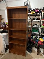 Front view of the 5-shelf adjustable bookcase in warm brown wood tone against garage background.