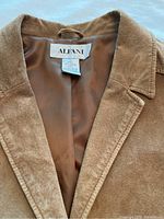 Close-up of the Alfani brand label inside the brown lined interior of the deep camel suede jacket.