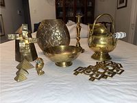 Photo showing entire brass collection on a table including windmill bank, vase, candle stick holder, coal scuttle, owl figurine, bowl, tapestry hangers, and stacking pyramids.